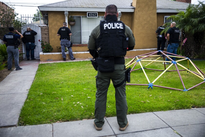 Persone che indossano giubbotti neri e camicie con la parola "POLIZIA STRADALE" su di loro stanno davanti a una casa.