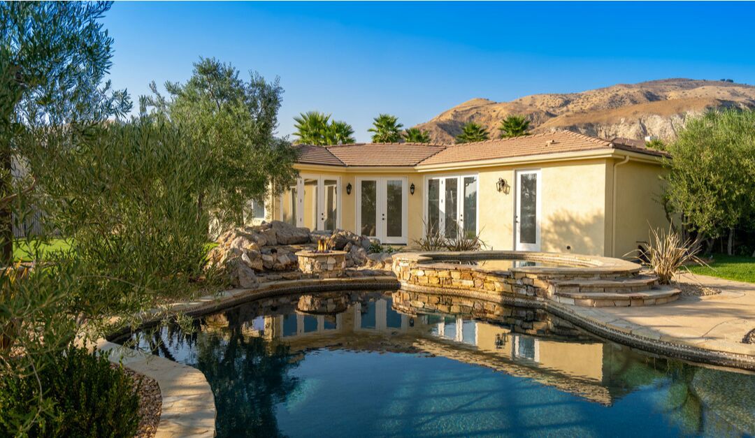 A closer view of the pool, spa and a portion of the home against a backdrop of hills.