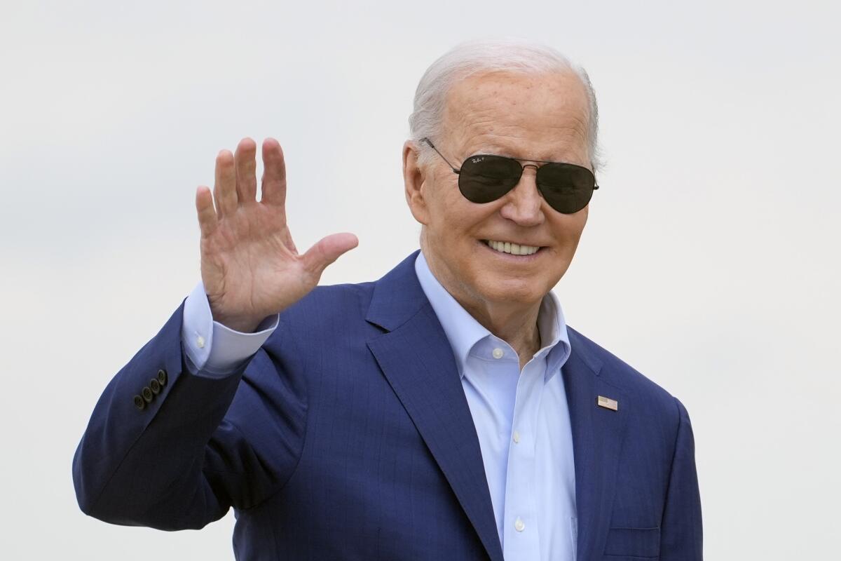 President Biden, wearing aviator sunglasses, smiles and waves.