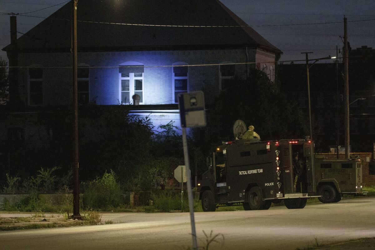 Police in armored trucks shine a spotlight on a building