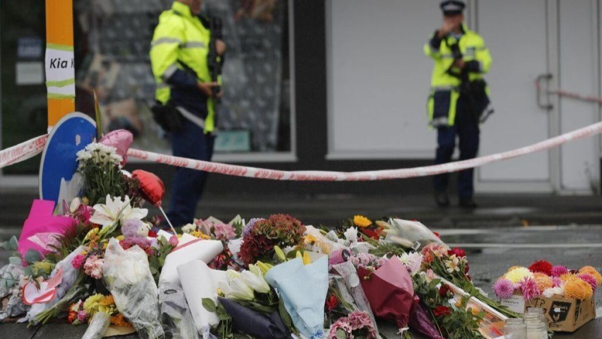 Flowers rest at a roadblock as two police officers stand guard by the makeshift memorial near the Linwood mosque in Christchurch, New Zealand, on Saturday. A 28-year-old white supremacist from Australia is accused in mass shootings at mosques that left 50 dead.