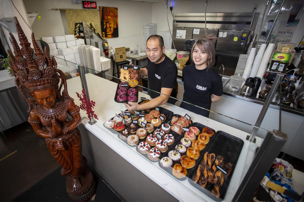 Two donut shop proprietors pose with their wares