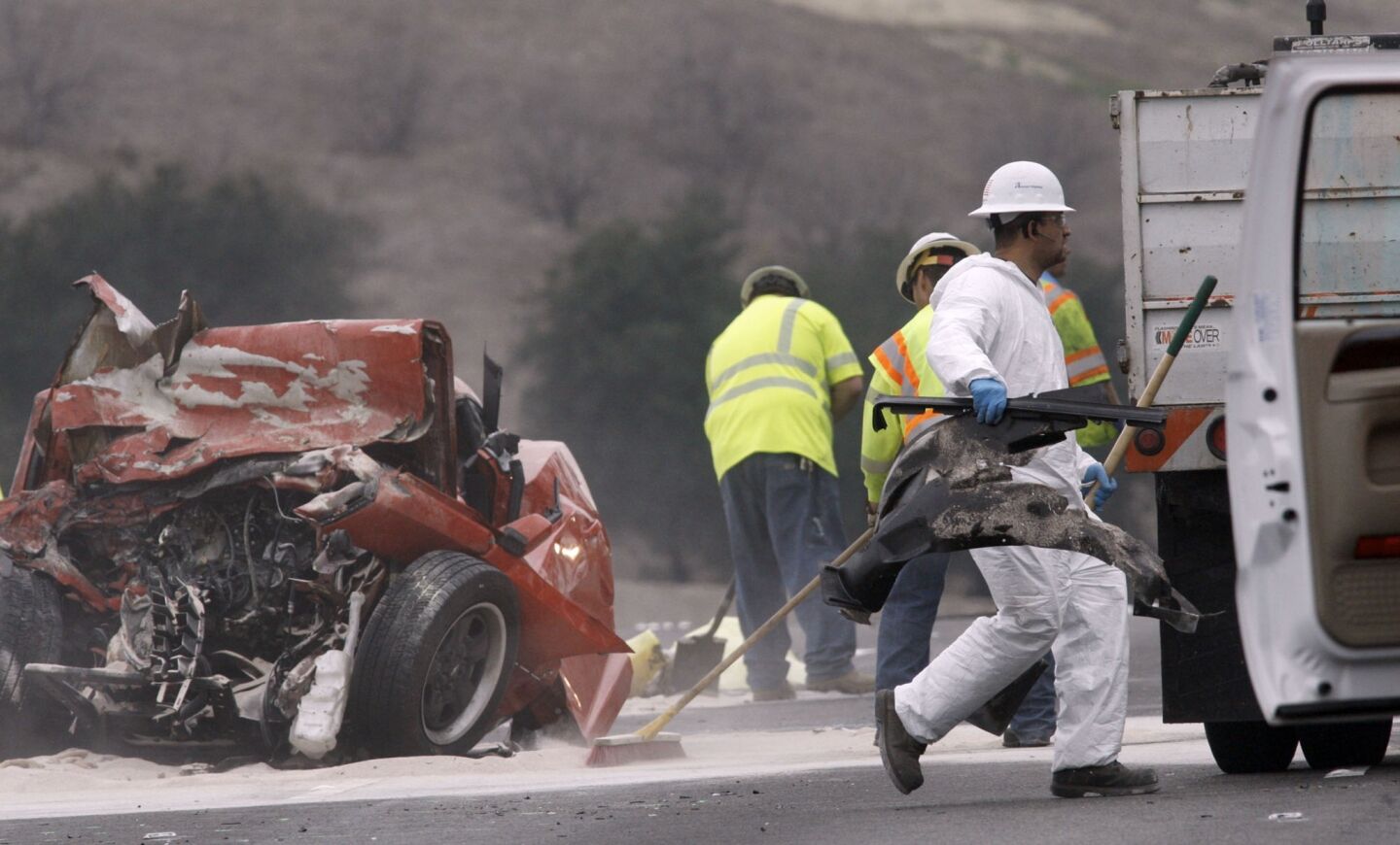 A worker removes debris from the wreckage of a car crash on the westbound 60 Freeway in Diamond Bar on Sunday.
