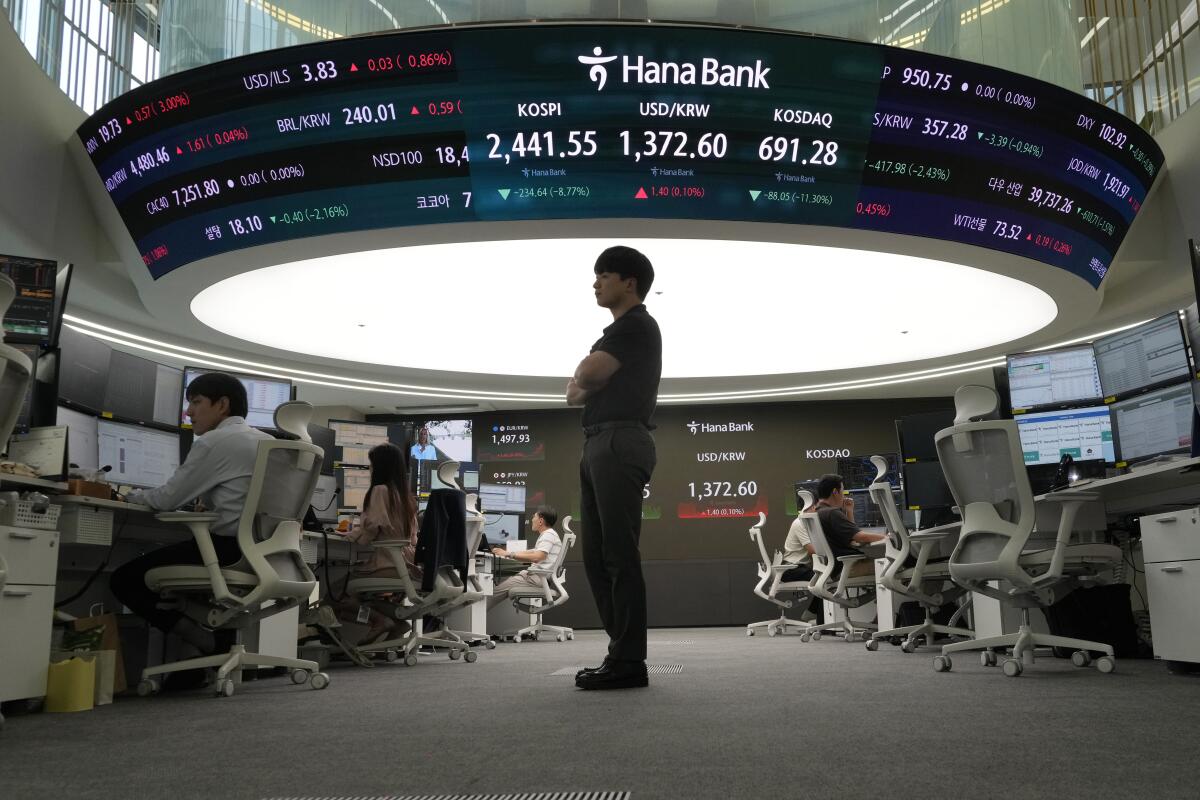 A person stands near screens showing stock index changes and foreign exchange rates