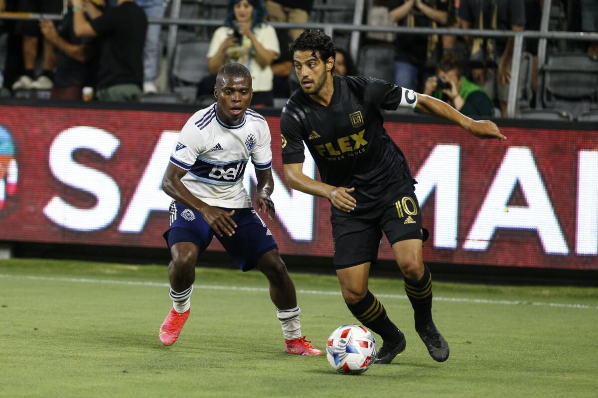 Carlos Vela of LAFC runs in front of the Vancouver Whitecaps' Deiber Caicedo during a soccer game.