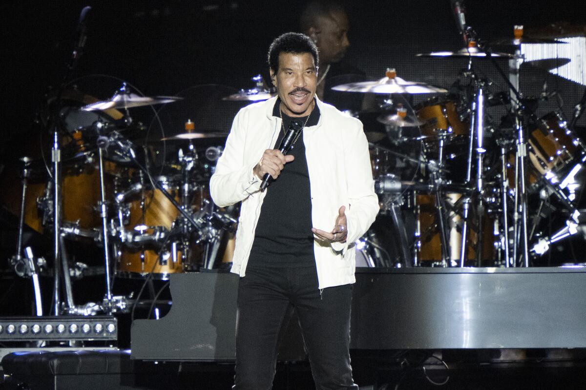 Lionel Richie performs in a white jacket over a black top and pants in Fool in Love.