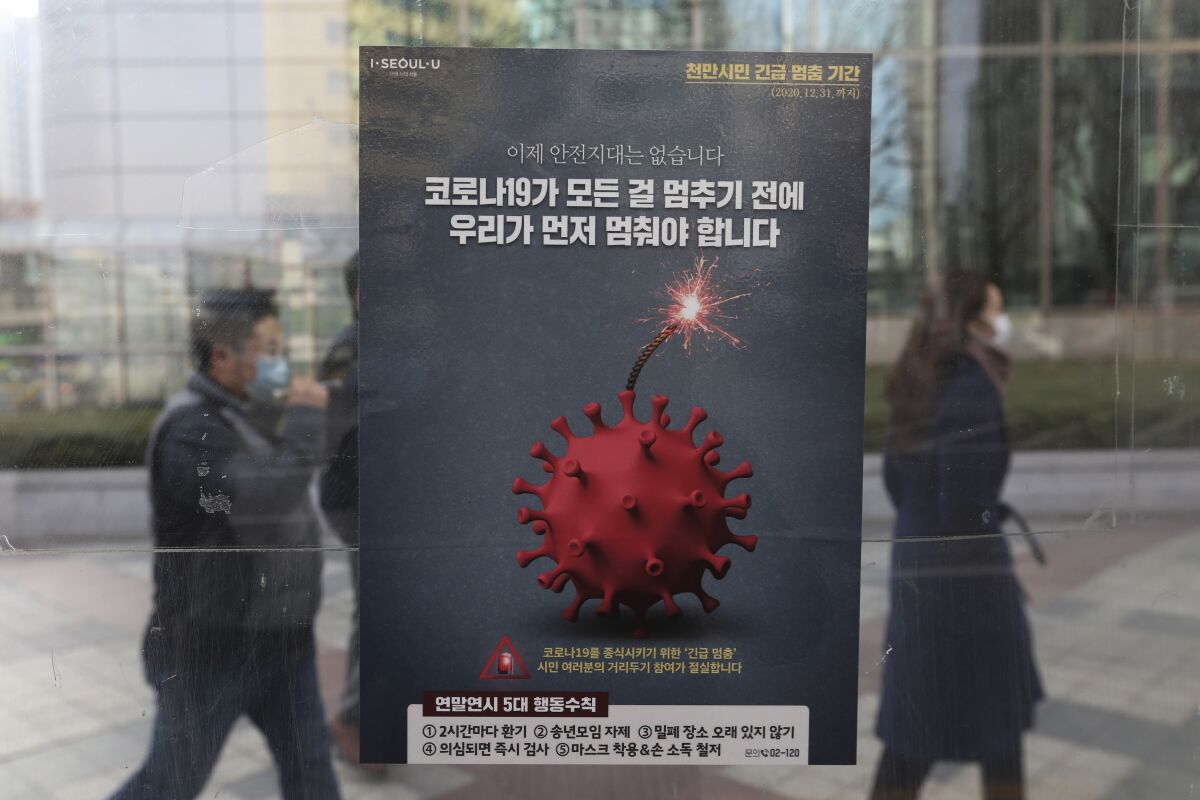 People wearing face masks as a precaution against the coronavirus pass by a poster emphasizing an enhanced social distancing campaign at a bus station in Seoul, South Korea, Monday, Dec. 7, 2020. South Korea's health minister said Monday that the Seoul metropolitan area is now a "COVID-19 war zone," as the country reported another 615 new infections and the virus appeared to be spreading faster. The signs read: "We have to stop before COVID-19 stops everything." (AP Photo/Ahn Young-joon)
