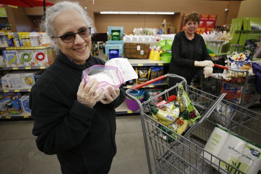 ALTADENA, CA - MARCH 19, 2020 Shopper Aviva Rosenbloom, 72, left, is thankful for toilet paper donated in single rolls by shopper Carol Wallace, right, who was able to grab a package early at the Grocery Outlet Bargain Market in Altadena as senior shoppers lined up before dawn outside Thursday morning as the store opened before 7am to accommodate the senior population. The store which normally opens at 9am said they wouldn't turn any person away but were allowing 30 shoppers in the store at a time to not exceed the 50 person recommended limit including staff. The store also had volunteers who took shopping lists from seniors in their vehicles to shop for them and return the items to them. (Al Seib / Los Angeles Times)