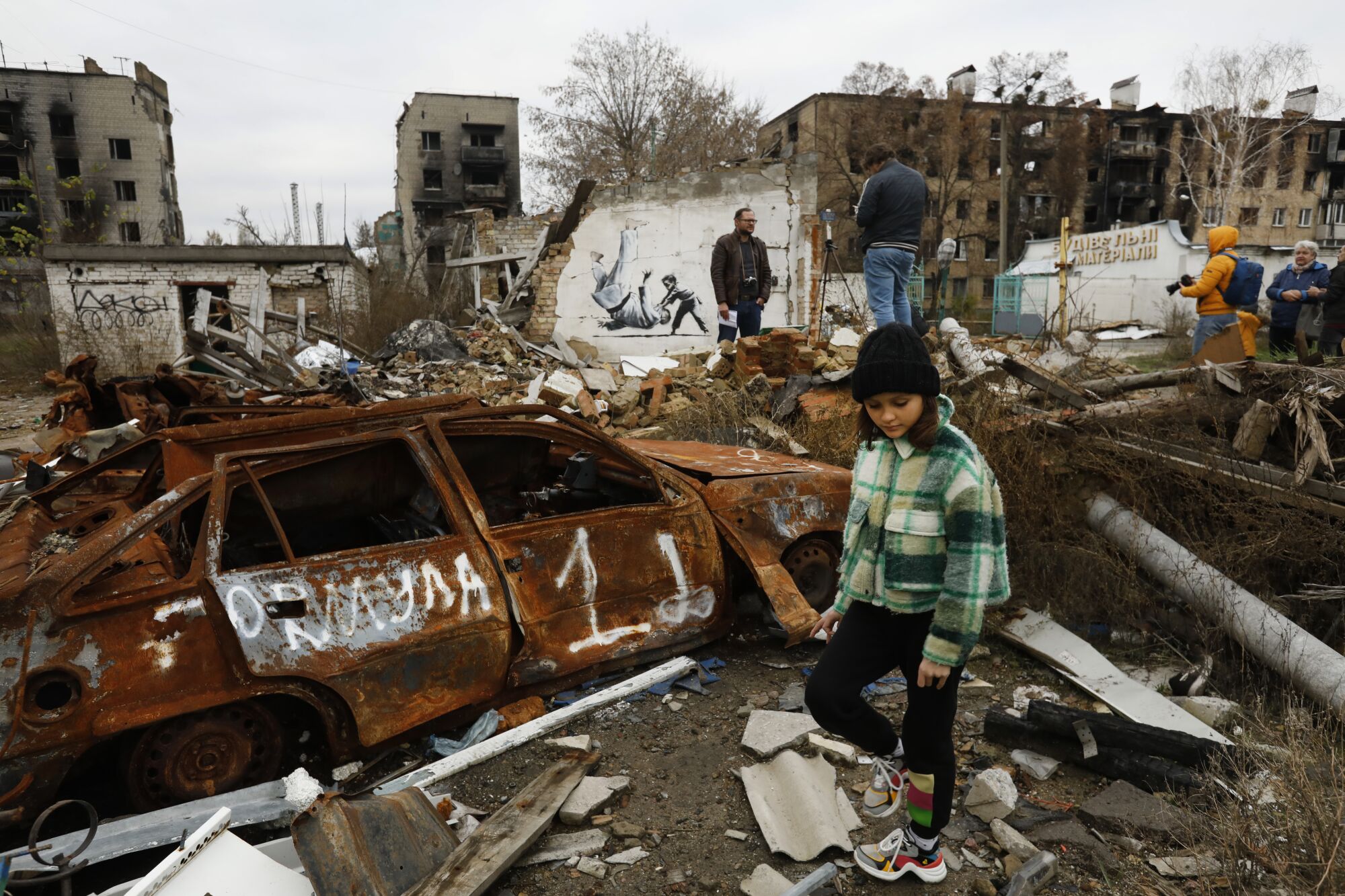 People in a rubble-filled yard with a mural in the background 