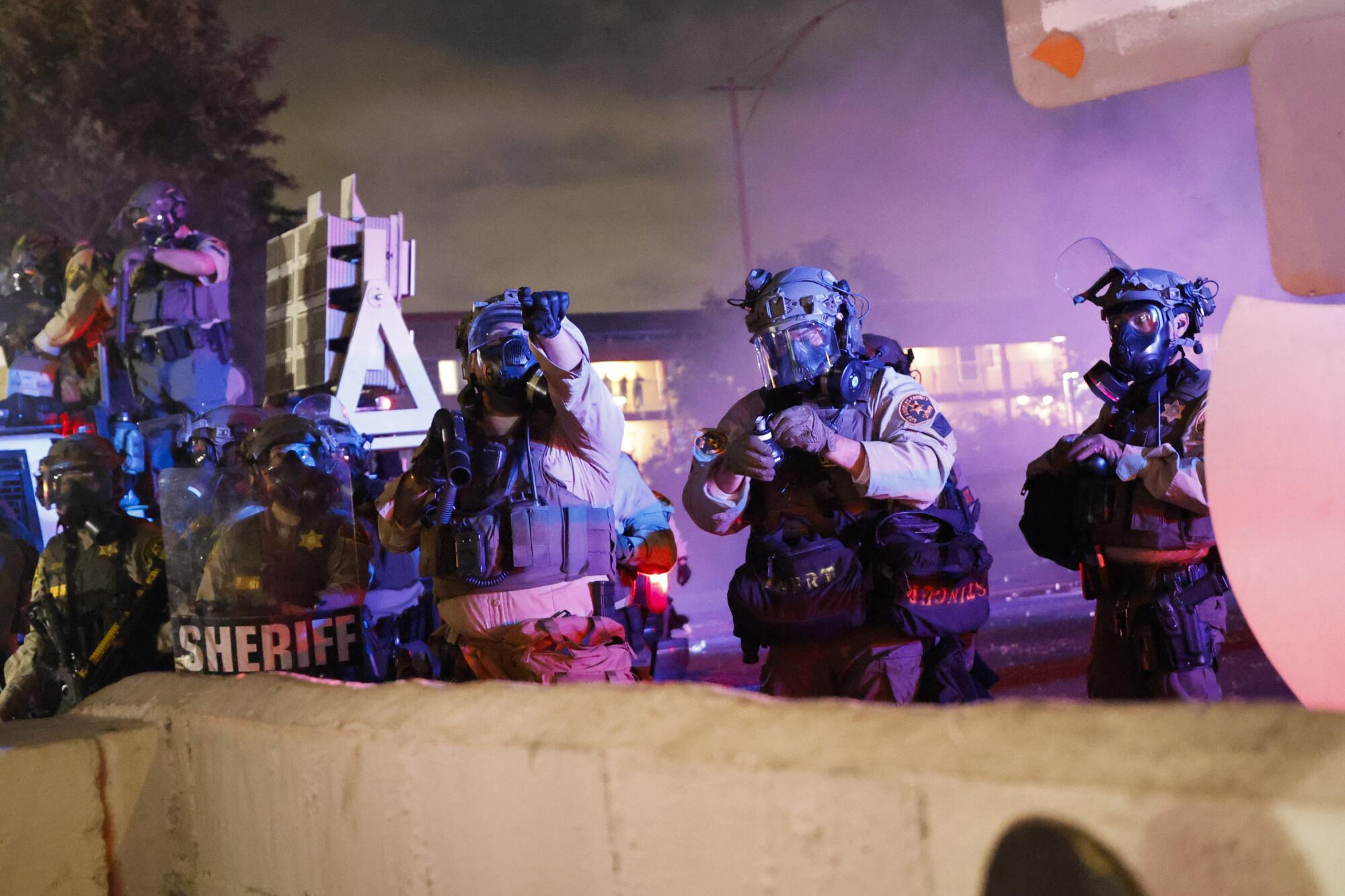 a line of sheriffs deputies wear tactical gear behind a barricade
