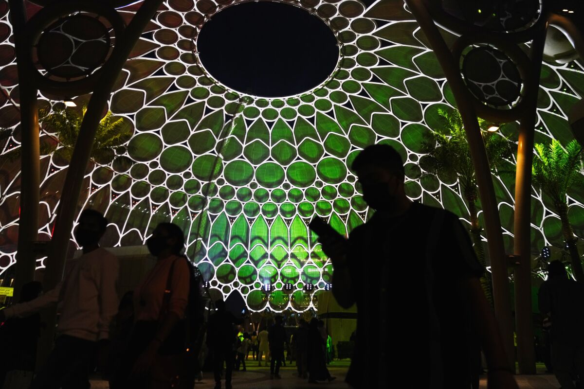 People walk past the Al Wasl Dome as it is lit at night at Expo 2020 in Dubai, United Arab Emirates, Friday, Oct. 1, 2021. After eight years of planning and billions of dollars in spending, the Middle East's first ever World Fair opened on Friday in Dubai, with hopes the months-long extravaganza draws both visitors and global attention to this desert-turned-dreamscape. (AP Photo/Jon Gambrell)