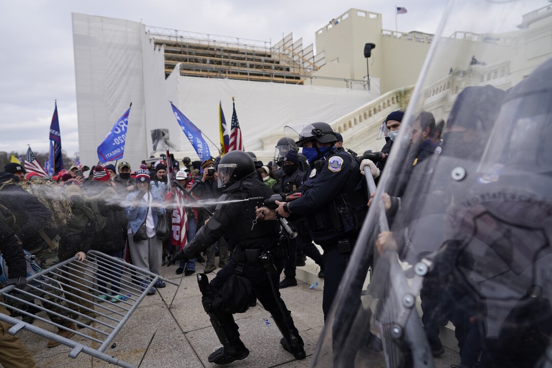 A police officers aims a stream of pepper spray toward a crowd of rioters. 