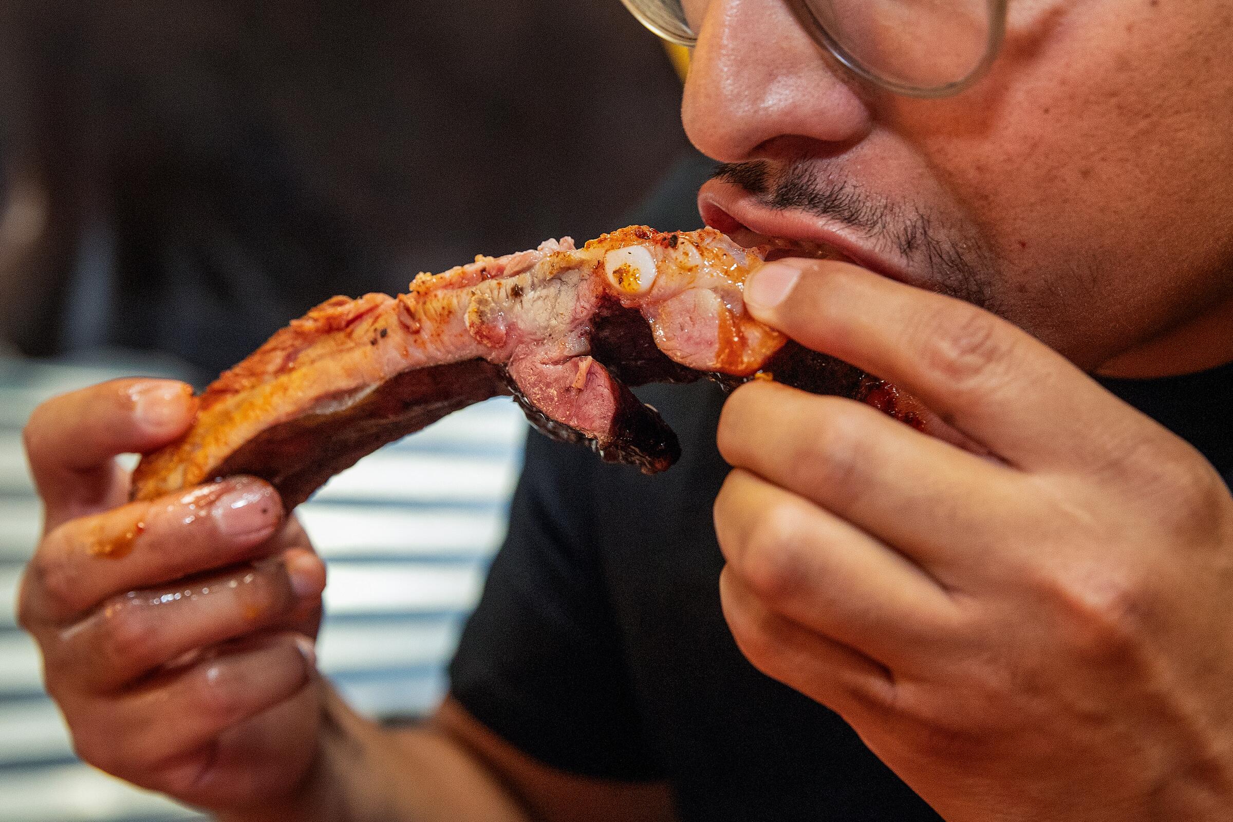 A person bites into a barbecued pork rib
