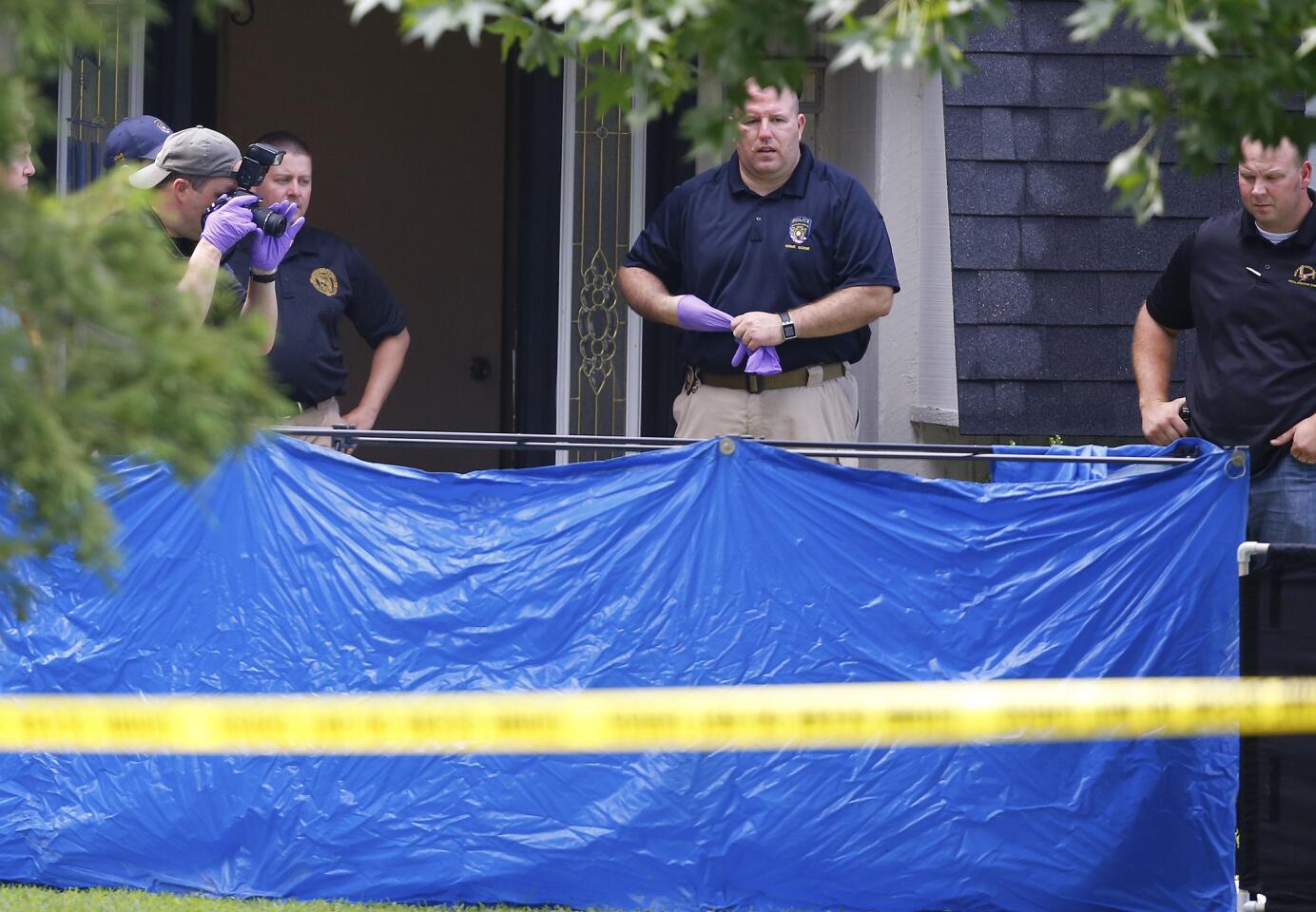 An investigator photographs behind a tarp in the frontyard of the home in Broken Arrow where five family members were found stabbed to death.
