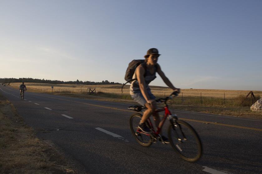 Cyclists ride down Hagar Drive onto College Drive on their way from the UCSC upper campus to the city of Santa Cruz Calif. on Thursday June 7, 2018. The university is proposing to build student housing on the lower East Meadow, at immediate right, as it struggles to accommodate demands to increase enrollment. (David Royal for the Los Angeles Times)