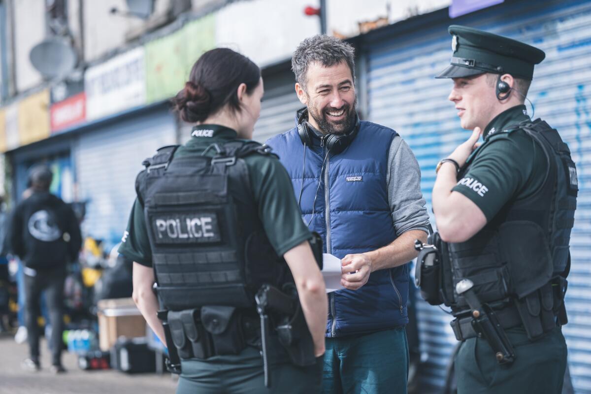 Adam Patterson is flanked by actors Annie Conlon, left, and Nathan Braniff, wearing police garb on a Belfast sidewalk