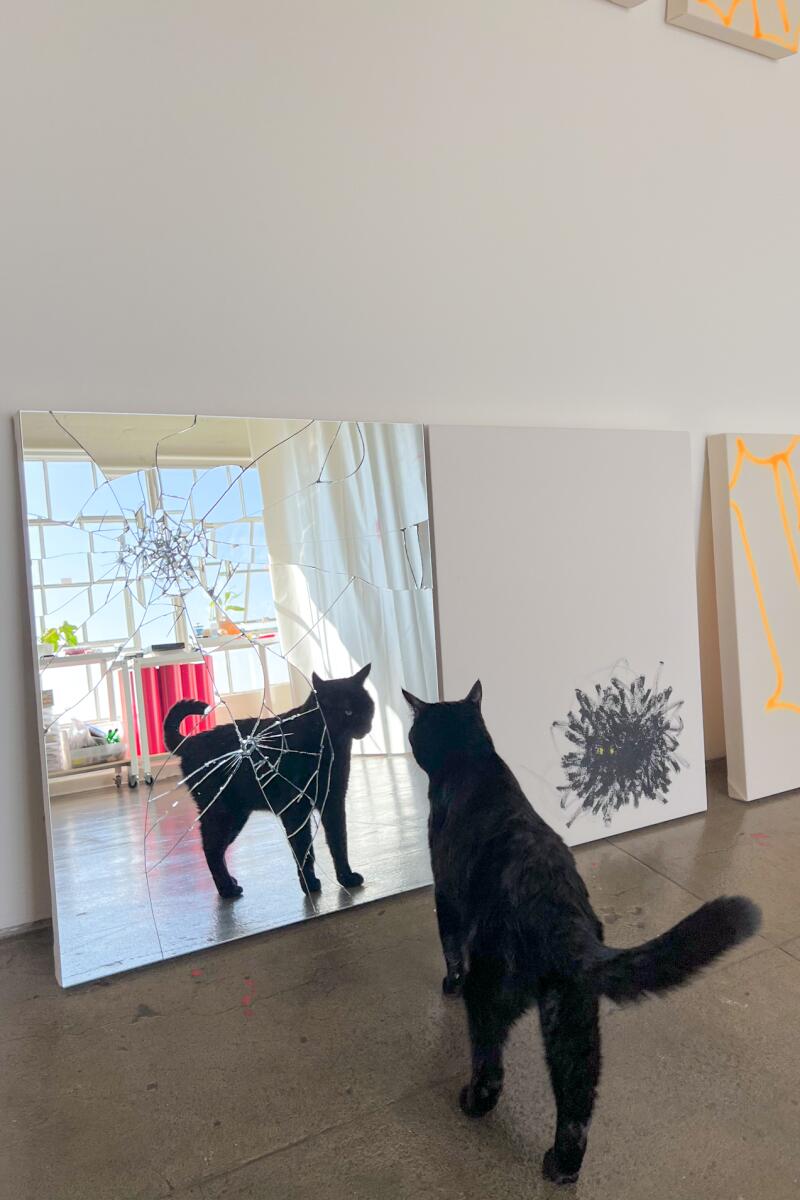 A black cat looking at artwork of a black cat.
