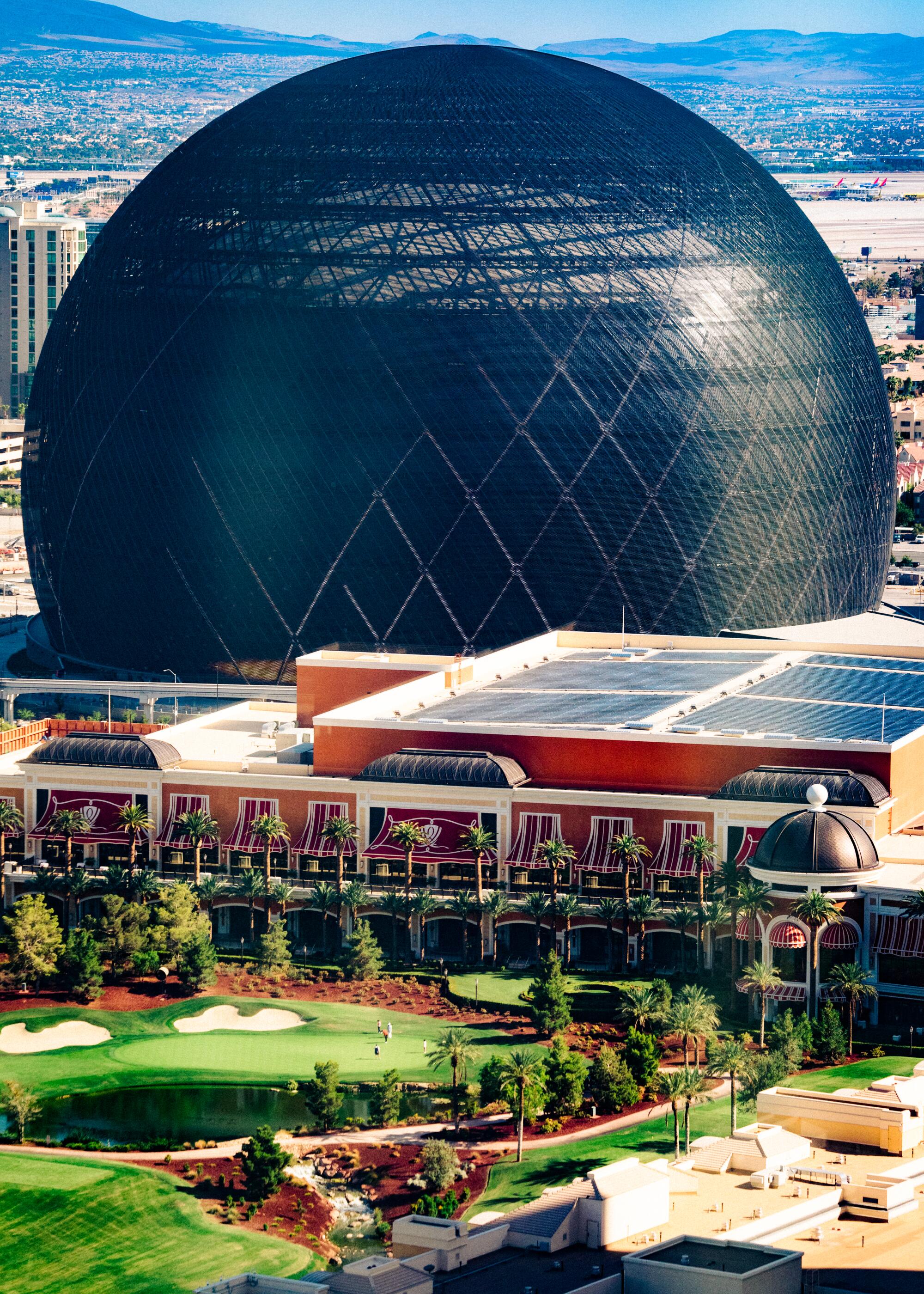 A large black spherical building is seen in daytime looming over the Wynn Golf Course.