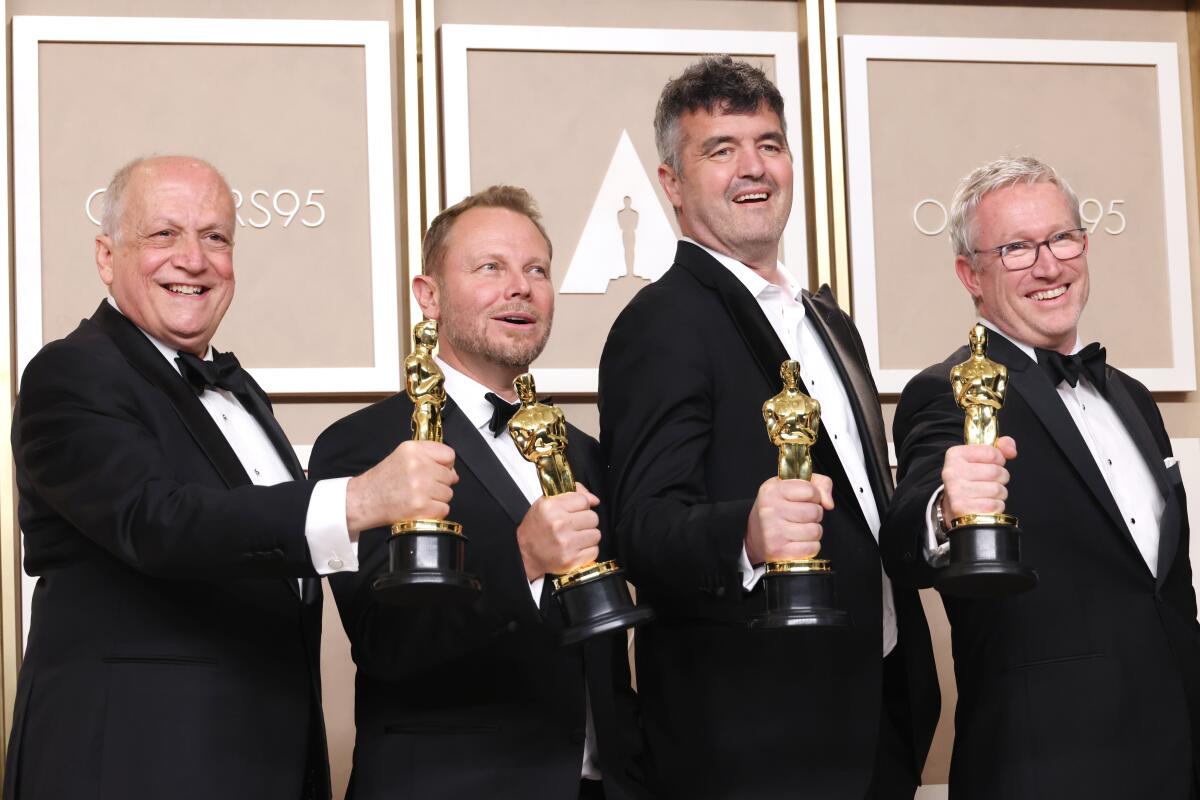 Four smiling men in tuxedos each hold their Oscars out with one hand