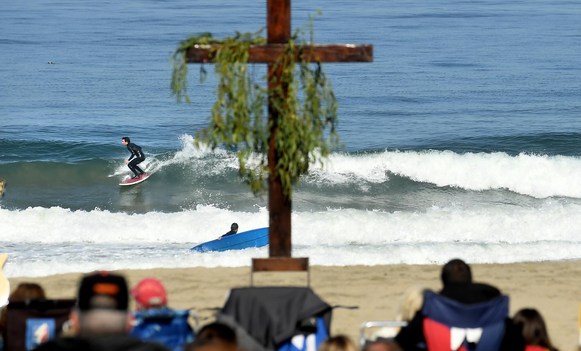 A cross on a beach as surfers appear in the background.