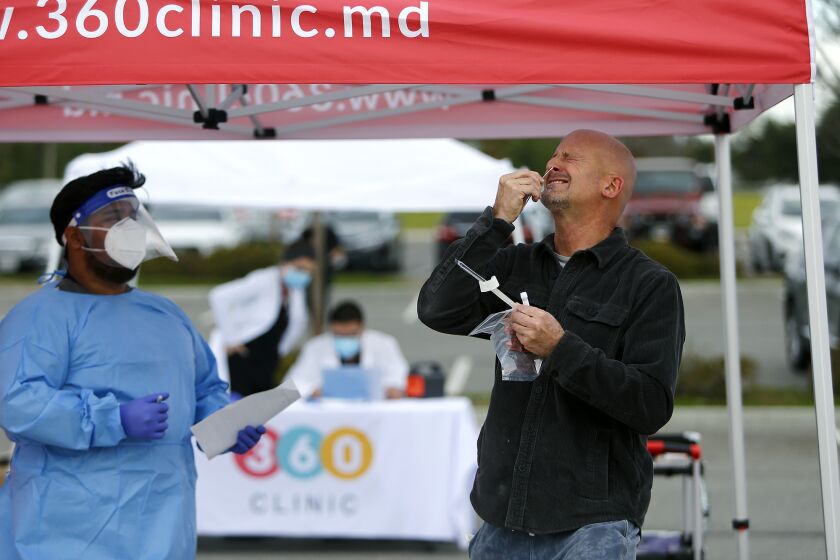 Tim Kersey, fire prevention analyst with the Fountain Valley Fire Department, swabs the inside of his nose as Clinic 360 medical assistant Angel Gonzalez screens him during a COVID-19 mobile testing site at Fountain Valley Sports Park on Tuesday morning.