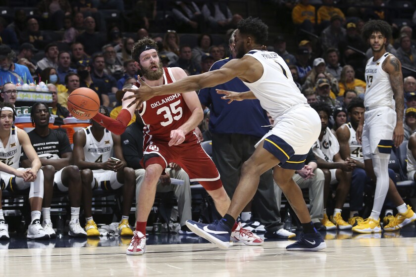 Oklahoma forward Tanner Groves (35) passes while defended by West Virginia forward Pauly Paulicap (1) during the first half of an NCAA college basketball game in Morgantown, W.Va., Wednesday, Jan. 26, 2022. (AP Photo/Kathleen Batten)