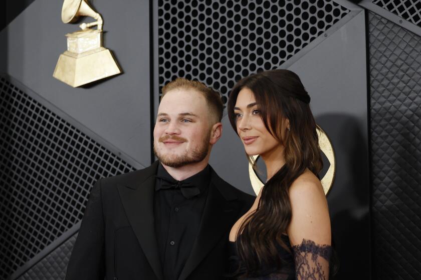 Zach Bryan in an all-black suit and Brianna "Chickenfry" LaPaglia in a black gown on the red carpet at 2024 Grammys