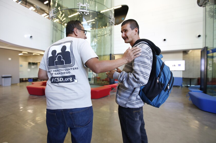 Homeless services navigator Jorge Mendoza, left, talks with Michael Cuarisma at the city's newly opened Housing Navigation Center on Monday. The one-stop shop for homeless services and resources is in a former Indoor Skydiving building in downtown San Diego, and the large tubes once used for the activity can be seen in the background.