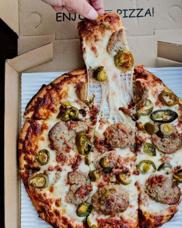 A hand pulls a square slice of meatball-and-jalape?o-topped tavern style pizza at Rance's Chicago Pizza in Long Beach