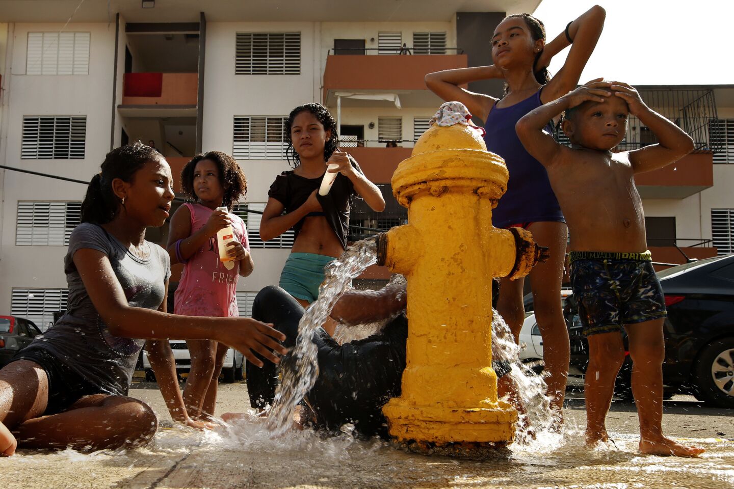 Children bath with the water from a fire hydrant in a public housing project in San Juan. Residents are still trying to get the basics of food, water, gas, and money from banks.