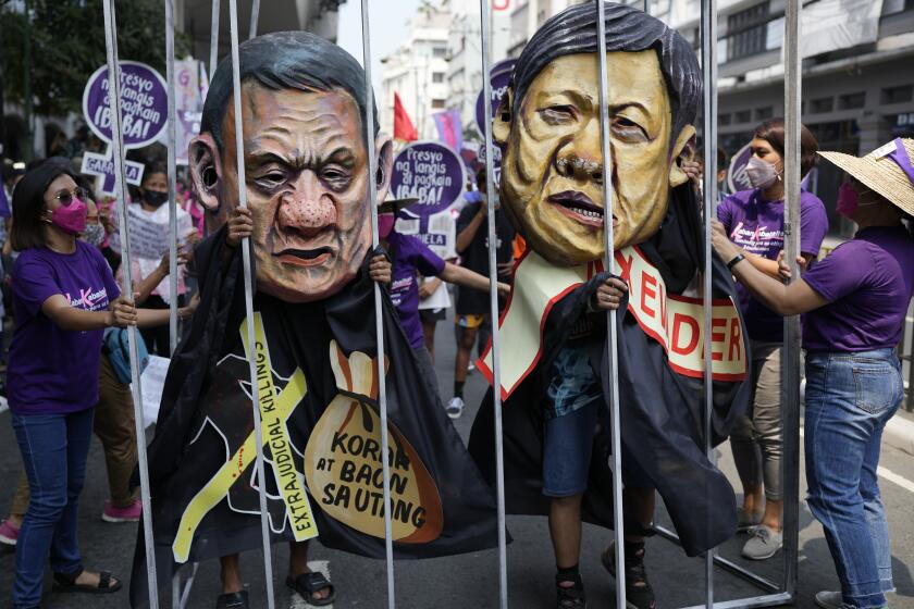 Protesters wearing masks portraying Philippine President Rodrigo Duterte, left, and former senator Ferdinand "Bongbong" Marcos Jr., the son of the late dictator Ferdinand Marcos, stands behind a mock jail during a rally near the Malacanang presidential palace in Manila, Philippines as they mark International Women's Day on Tuesday, March 8, 2022. (AP Photo/Aaron Favila)