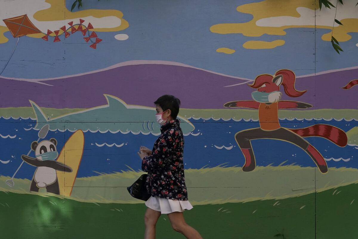 Un transeúnte porta una mascarilla mientras camina frente a un mural durante la pandemia