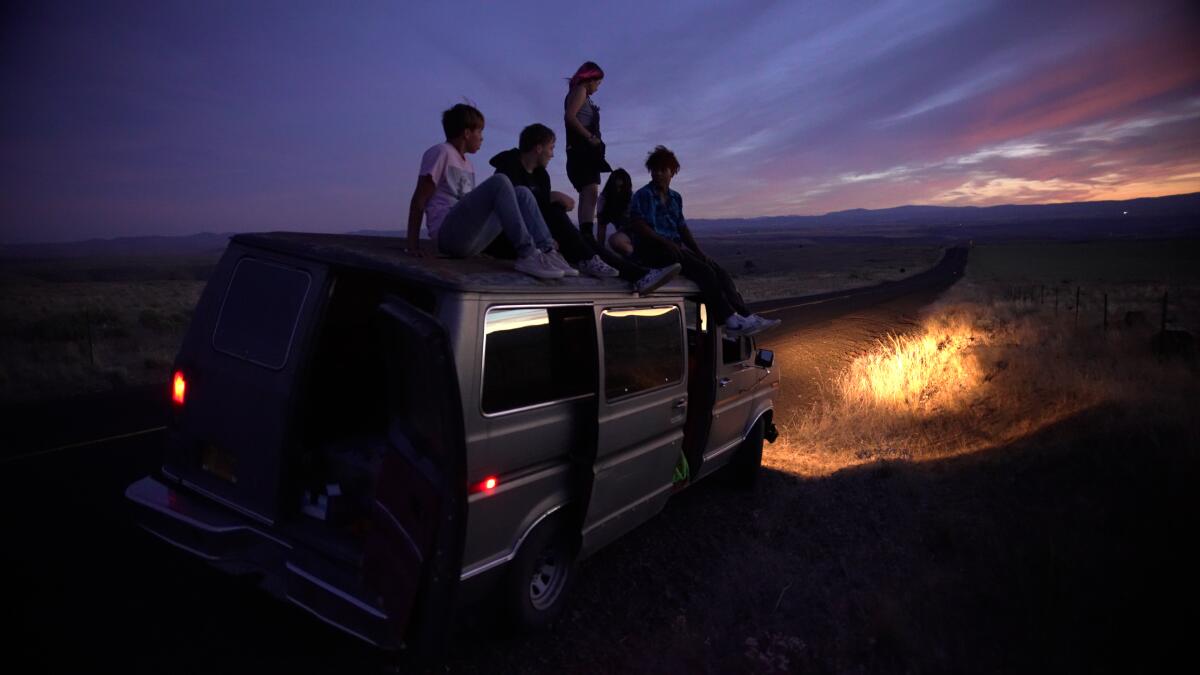 Several friends sit on the top of a van at night.