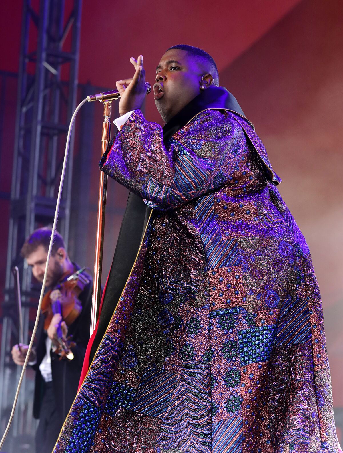Un hombre con un abrigo de brocado canta en un micrófono