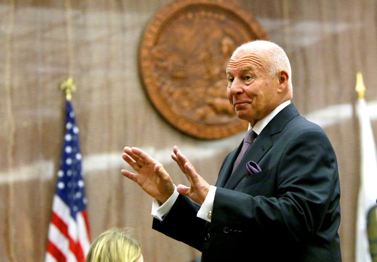 A man gestures from a courtroom, with an American flag behind him.