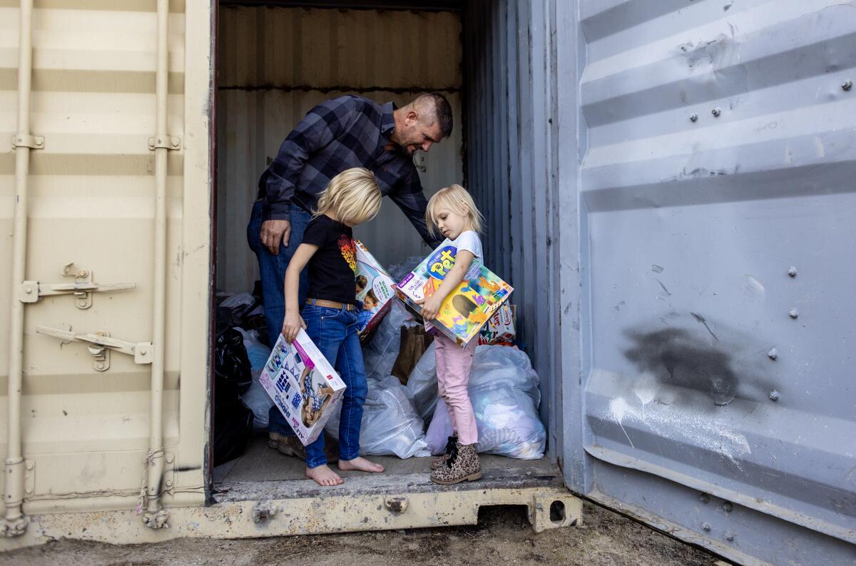 A man and two girls who are holding toys in the entrance to a shipping container.