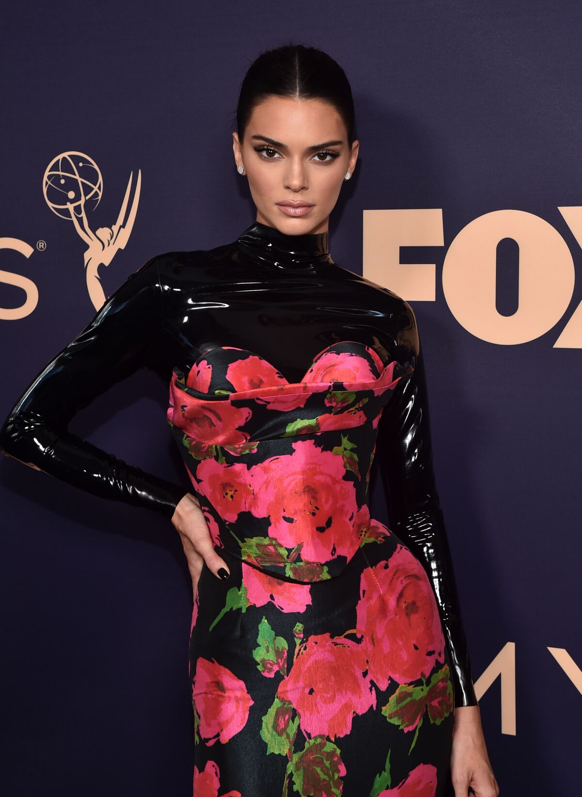 Kendall Jenner poses with her hand on her hip, wearing a latex and floral gown