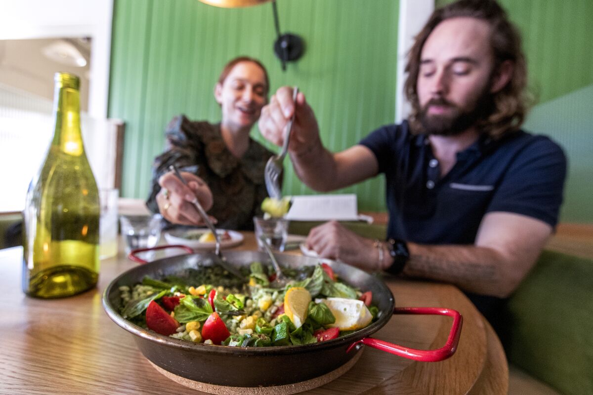 A woman and a man sit at a restaurant table eating vegetarian paella, which is in a metal pan on the table