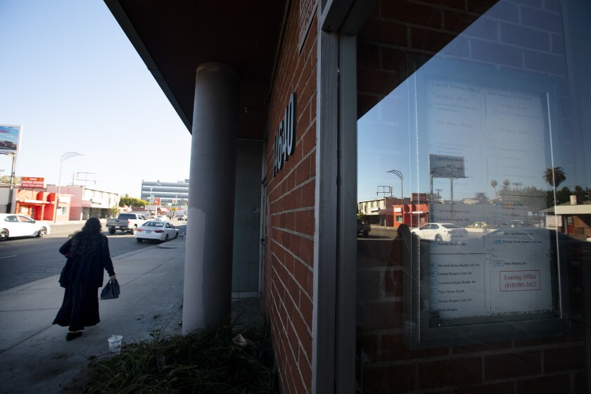 A pedestrian walks on a sidewalk outside a low-slung office building in the San Fernando Valley