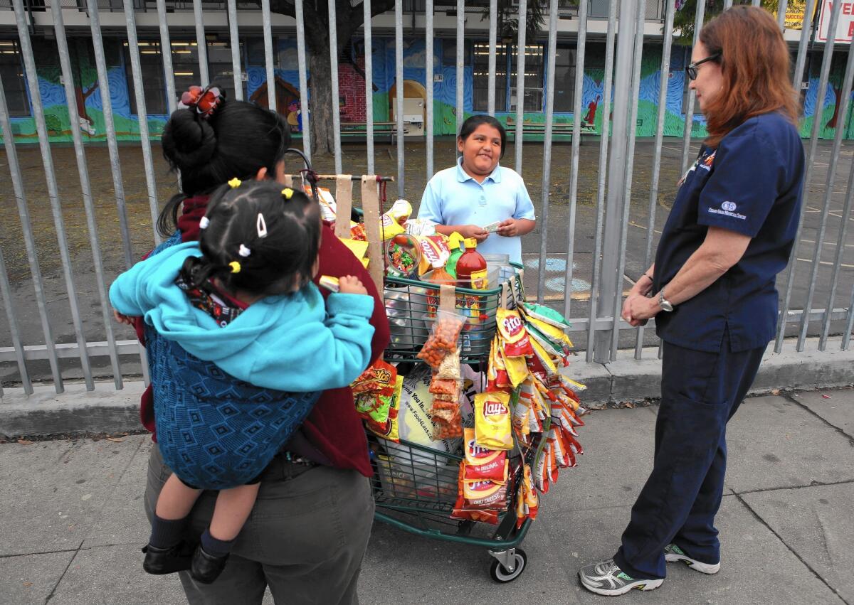 Nurse practitioner Anne Traynor, right, advises 8-year-old Dafne Sanchez, center, who wanted to buy junk food from a vendor after she got a health checkup in a Cedars-Sinai mobile clinic visiting the Jordan Downs housing project in South Los Angeles.