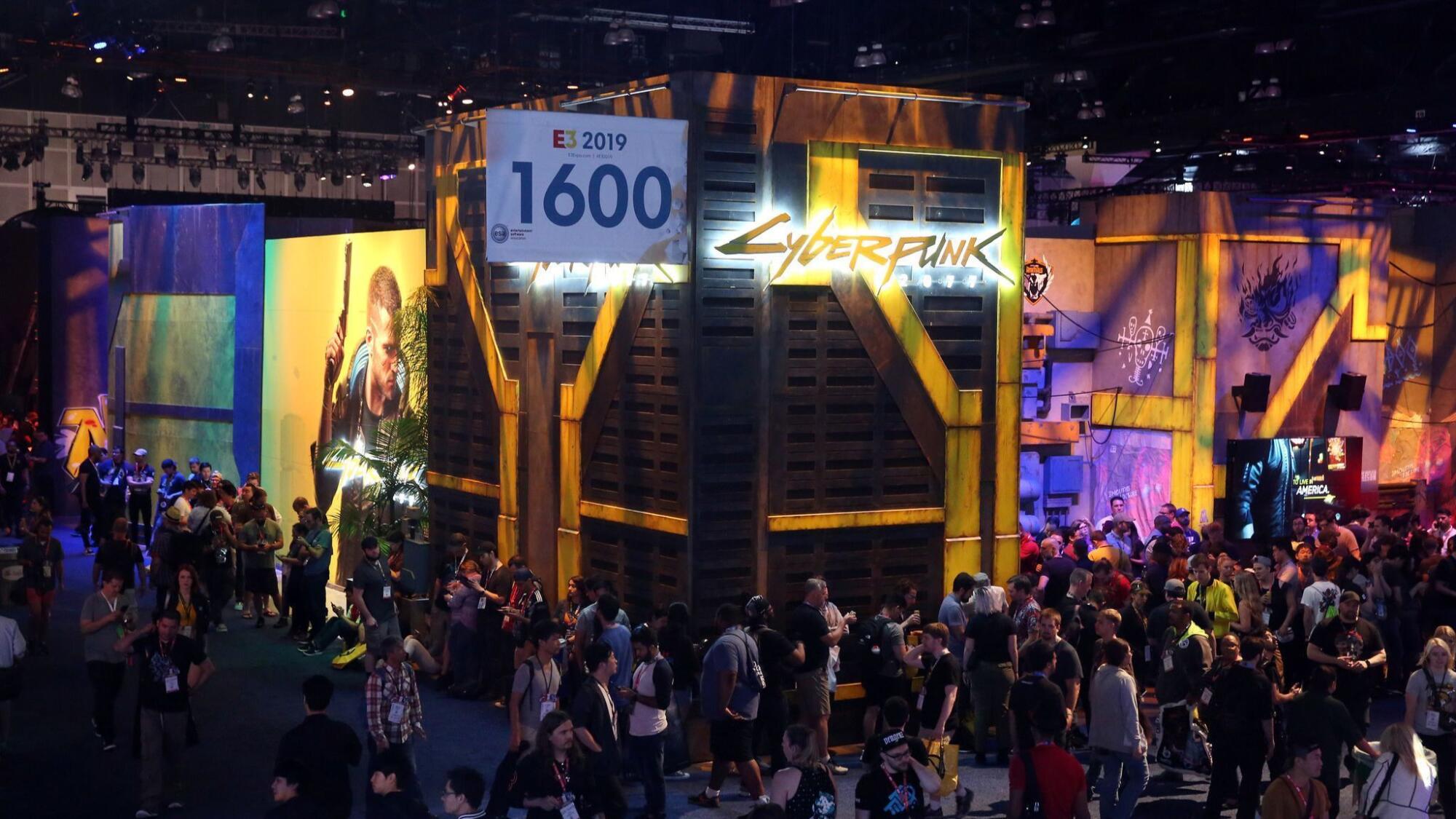 A crowd files past brightly lighted displays in a convention hall