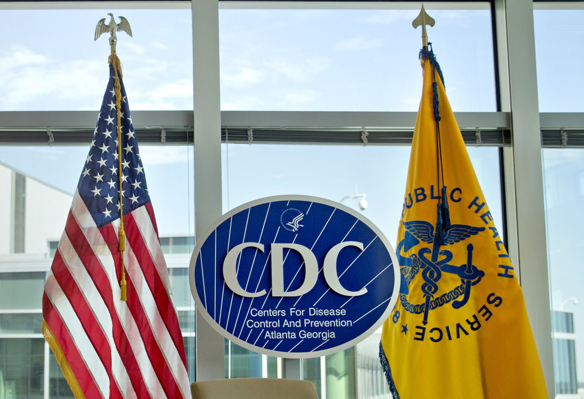 The U.S. flag, left, and a yellow flag depicting a blue caduceus flank a blue oval-shaped CDC logo 