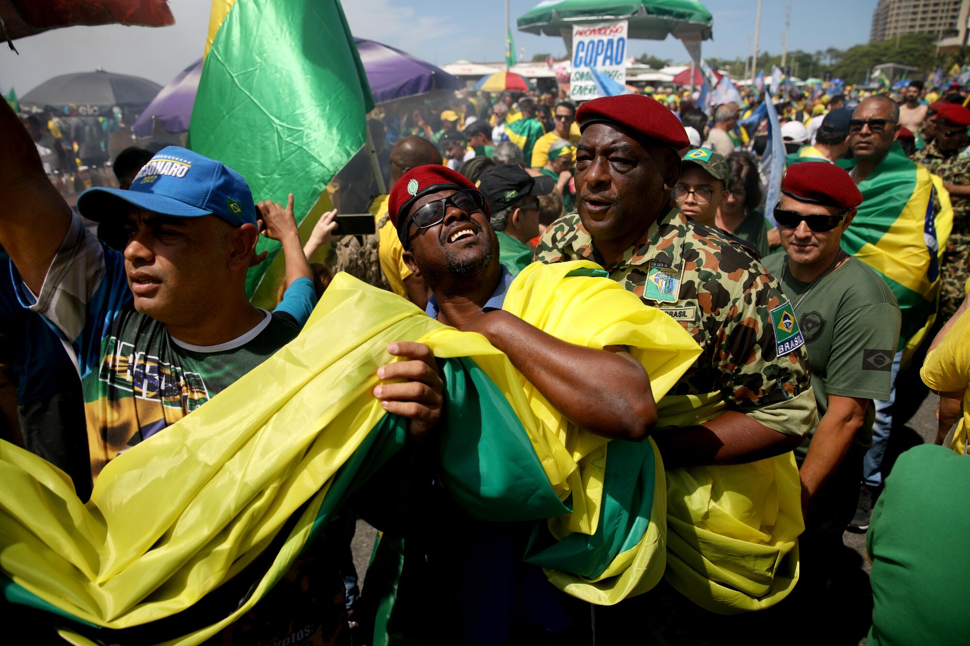 Men in red berets join other people carrying a large swath of yellow-and-green cloth 