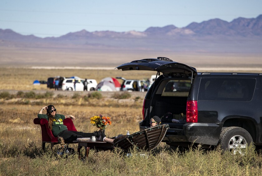 Two people sitting on chairs next to an SUV in the desert