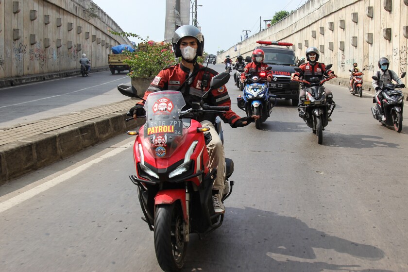 Motorcyclists in red-and-black jackets lead an ambulance. 