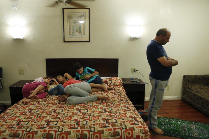 Fouad Wawieh, right, prays in his family's motel room in Pomona as four of his six children -- Maram, 9, left; Massa, 5; Omar, 19; and Omran, 12 -- use the family's smartphones. The family escaped from Syria via Egypt to arrive in the U.S.