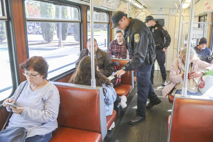 Transit officer Marc Vargas, who does code compliance transit enforcement for the San Diego Metropolitan Transit System, checks trolley riders for valid fares on the Green Line on January 9, 2020 in San Diego, California. In the background is transit officer Ramon Garcia who provides security for Vargas.