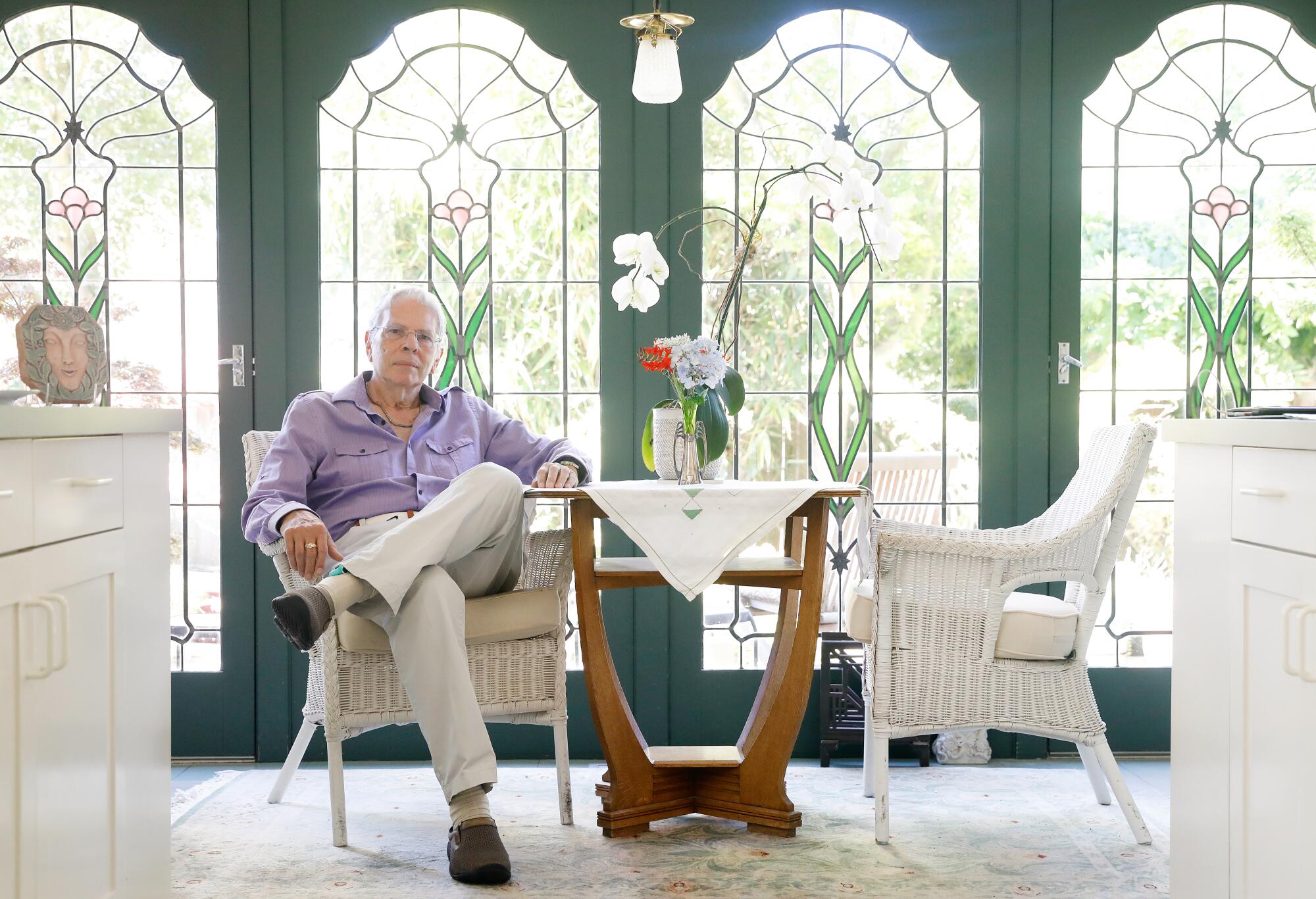 A portrait of Larry Kreisman sitting in a white wicker chair at home.