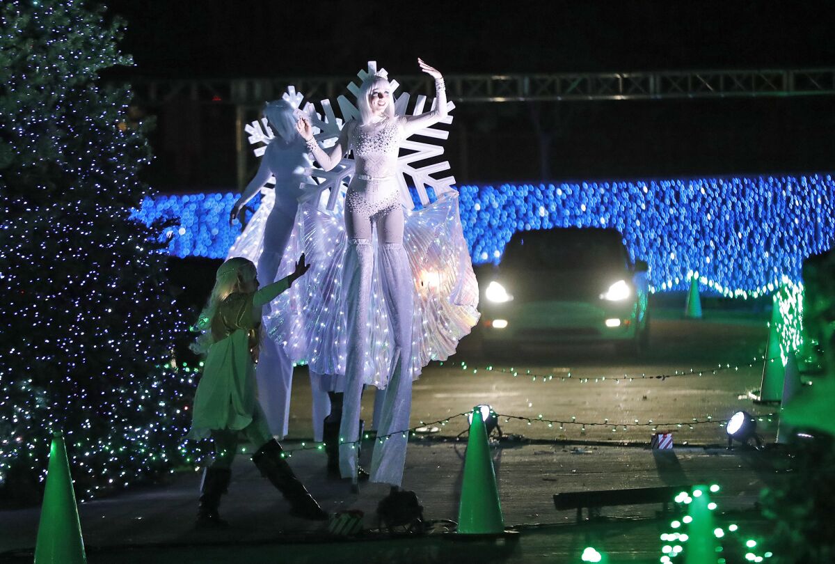 A snow angel on stilts waves to passing cars Tuesday during a preview of Night of Lights OC at Costa Mesa's O.C. fairgrounds.