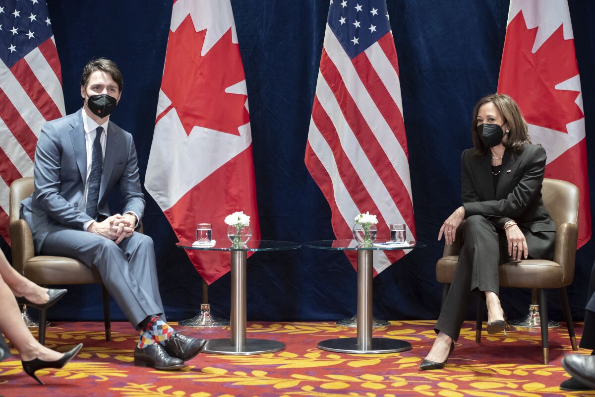 Vice President Kamala Harris sits next to Canadian Prime Minister Justin Trudeau with flags behind them.